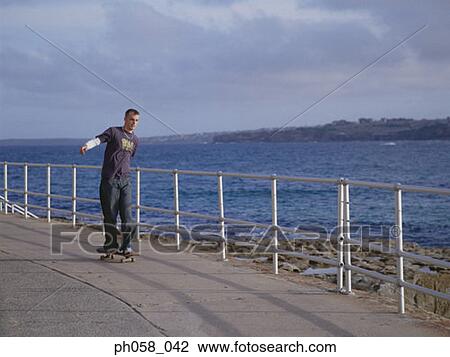 Young man skateboarding on pavement, near sea View Large Photo Image Stock Image - Young man skateboarding on pavement, near sea. Fotosearch