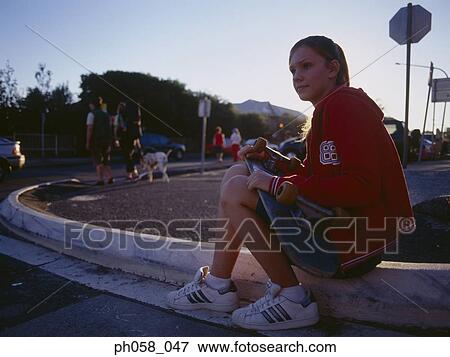Young woman sitting on curb holding a skateboard View Large Photo Image Stock Photo - Young woman sitting on curb holding a skateboard. Fotosearch