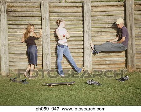 Stock Photo - Three young people posing in front of wooden fence. Fotosearch