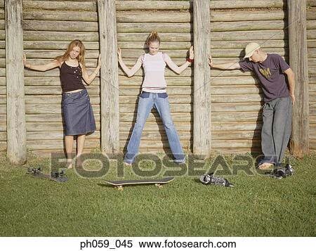 Stock Photography - Three young people posing in front of wooden fence. Fotosearch