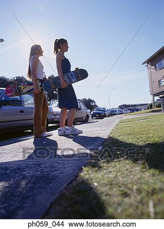 Picture - Two women walking on walkway holding skateboards, side view . Fotosearch