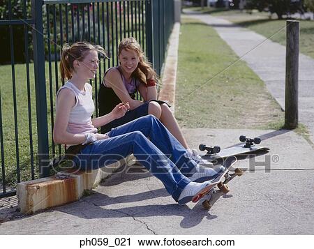 Stock Image - Two young women sitting on curb, chatting. Fotosearch