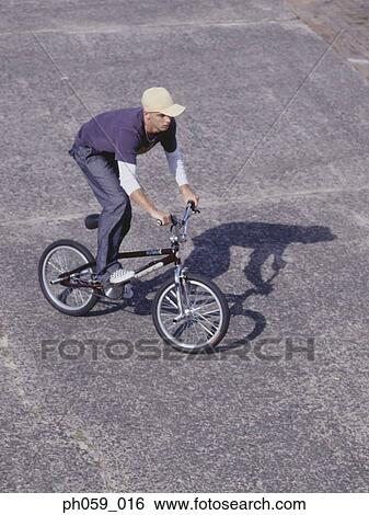 Young man cycling on walkway View Large Photo Image Stock Photograph - Young man cycling on walkway. Fotosearch