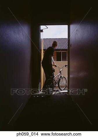 Picture - Young man pushing bike out of corridor. Fotosearch