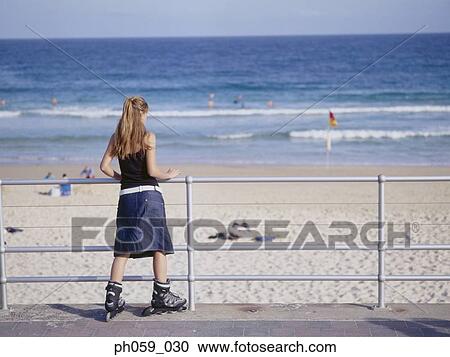 Stock Image - Young woman in inline skate leaning on railing, rear view. Fotosearch