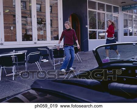 Stock Photo - Young woman skateboarding, friend behind her. Fotosearch