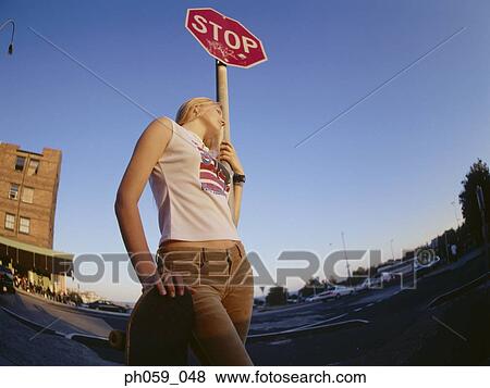 Stock Photo - Young woman standing near stop sign, looking away. Fotosearch