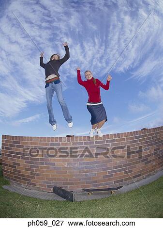 Stock Photo - Young women jumping from wall, arms outstretched . Fotosearch