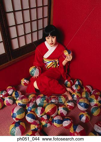 Picture - Japanese woman in kimono crouching against wall, room full of paper balls. Fotosearch