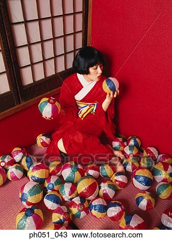 Stock Image - Japanese woman in kimono crouching against wall, room full of paper balls. Fotosearch
