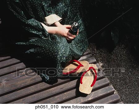 Stock Image - Woman holding a bottle and a pair of Japanese clogs. Fotosearch