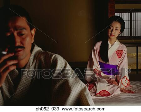 Stock Photo - Japanese couple on bed, man with cigarette. Fotosearch