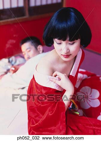 Stock Image - Japanese couple on bed, woman removing kimono. Fotosearch