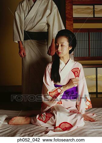 Stock Image - Traditional Japanese couple, woman sitting on mattress, man standing . Fotosearch