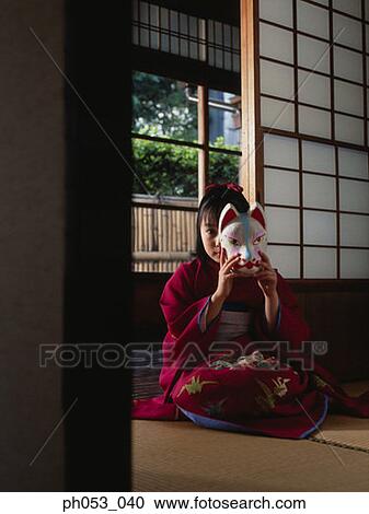Stock Image - Japanese girl in kimono holding a mask. Fotosearch