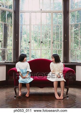 Two girls on a sofa, looking at each other View Large Photo Image Stock Image - Two girls on a sofa, looking at each other. Fotosearch