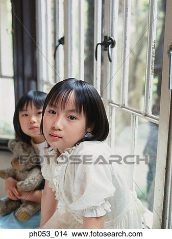 Picture - Two girls sitting on window ledge, portrait. Fotosearch