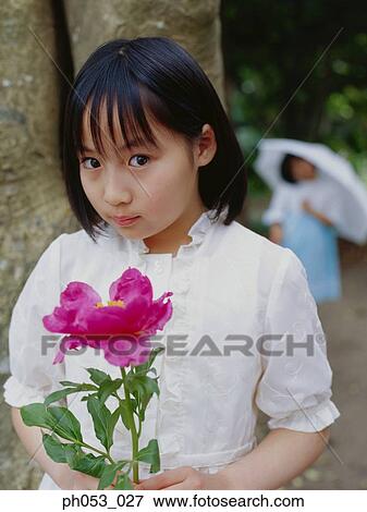 Young girl holding flower, another girl with umbrella in background View Large Photo Image Stock Photo - Young girl holding flower, another girl with umbrella in background. Fotosearch