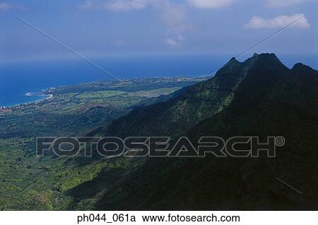 Stock Image - Aerial view of lush green mountains jutting out into the ocean, Kauai, Hawaii . Fotosearch