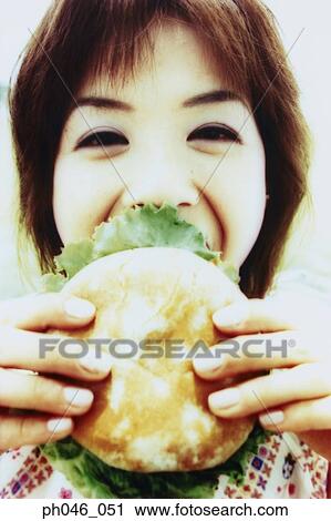Young woman biting into hamburger View Large Photo Image Stock Image - Young woman biting into hamburger. Fotosearch