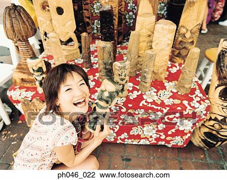 Stock Image - Young woman holding Hawaiian handicraft, smiling. Fotosearch