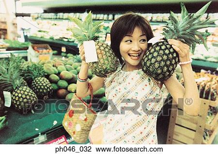Stock Image - Young woman holding pineapples in fruit store. Fotosearch