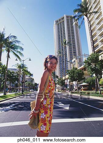 Stock Image - Young woman standing on urban sidewalk, smiling, portrait . Fotosearch