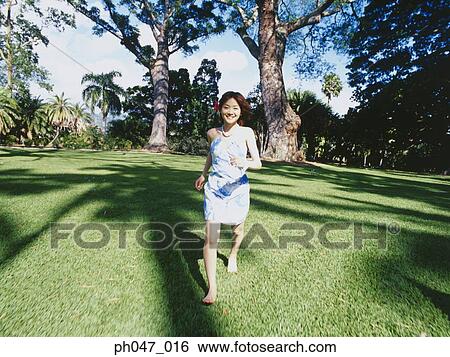 Stock Photograph - Young woman in Hawaiian blouse, running on lawn . Fotosearch