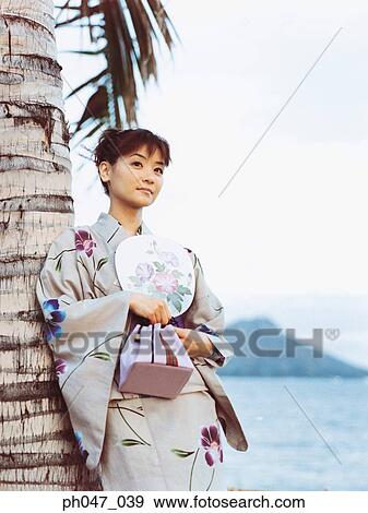Stock Photo - Young woman in Japanese kimono leaning on coconut tree, portrait. Fotosearch