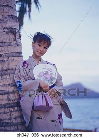 Stock Photograph - Young woman in Japanese kimono leaning on coconut tree, portrait. Fotosearch