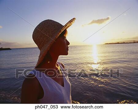 Stock Image - Young woman in straw hat at sunset, portrait. Fotosearch