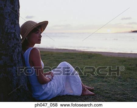 Young woman in straw hat sitting against tree at sunset View Large Photo Image Stock Photo - Young woman in straw hat sitting against tree at sunset. Fotosearch