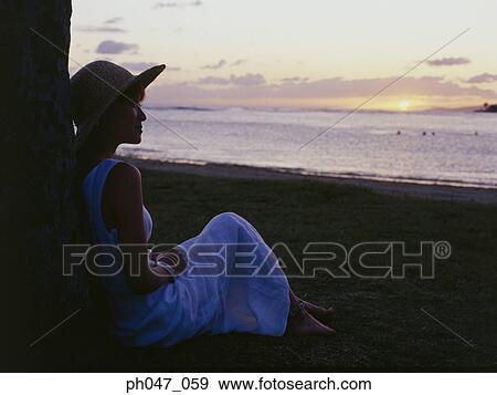 Young woman in straw hat sitting against tree at sunset View Large Photo Image Stock Photo - Young woman in straw hat sitting against tree at sunset. Fotosearch