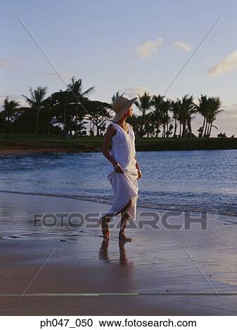 Stock Image - Young woman in straw hat walking on the beach, portrait. Fotosearch
