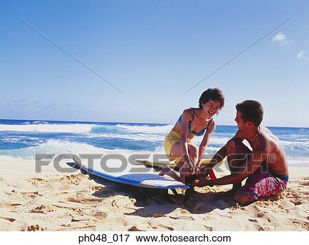 Young couple adjusting surfboard on beach View Large Photo Image Stock Photo - Young couple adjusting surfboard on beach. Fotosearch