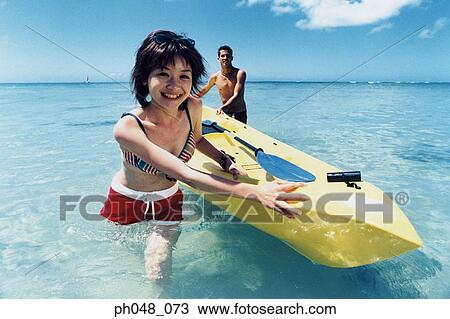 Stock Image - Young couple pulling kayak to shore. Fotosearch