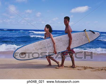 Stock Image - Young couple walking along a beach with surfboard . Fotosearch