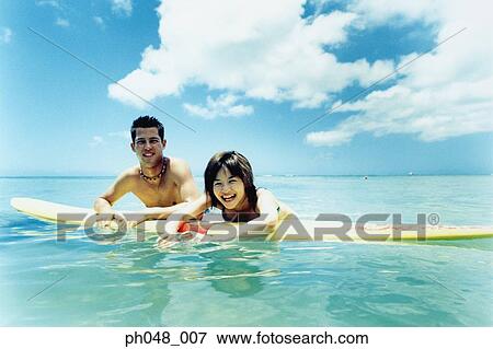 Stock Photo - Young man and woman on surfboard in water . Fotosearch