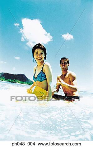 Picture - Young man and woman sitting on surfboard in water . Fotosearch