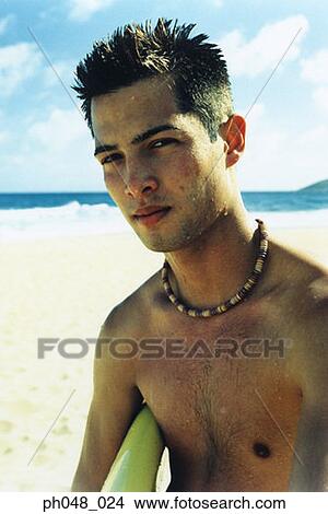 Young man at a beach, holding surfboard View Large Photo Image Picture - Young man at a beach, holding surfboard . Fotosearch