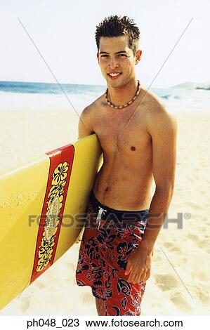 Young man at a beach, holding surfboard View Large Photo Image Stock Image - Young man at a beach, holding surfboard . Fotosearch
