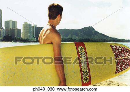 Young man at a beach, holding surfboard View Large Photo Image Stock Image - Young man at a beach, holding surfboard . Fotosearch