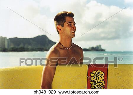 Stock Photo - Young man at a beach, holding surfboard . Fotosearch