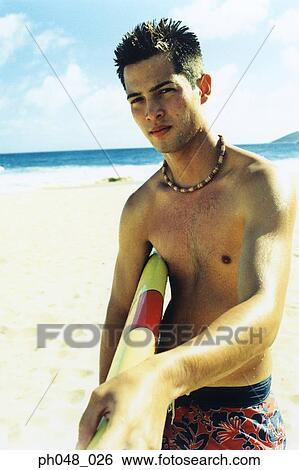 Stock Photograph - Young man at a beach, holding surfboard . Fotosearch
