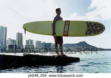 Young man at a platform, holding surfboard View Large Photo Image Picture - Young man at a platform, holding surfboard . Fotosearch
