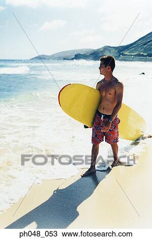Young man walking along a beach with surfboard View Large Photo Image Stock Image - Young man walking along a beach with surfboard . Fotosearch