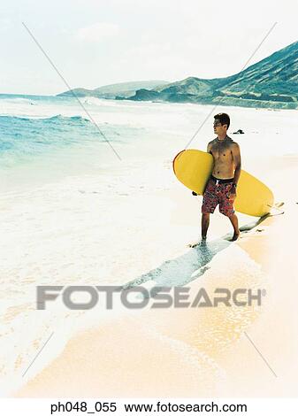 Stock Photography - Young man walking along a beach with surfboard . Fotosearch
