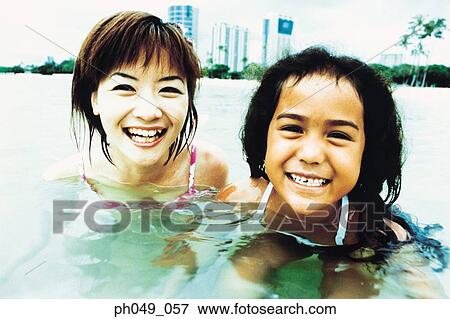 Stock Photo - Young woman and Hawaiian girl in shallow water, smiling. Fotosearch