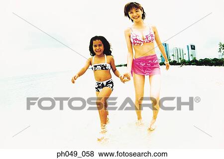 Stock Photo - Young woman and Hawaiian girl walking in shallow waters. Fotosearch