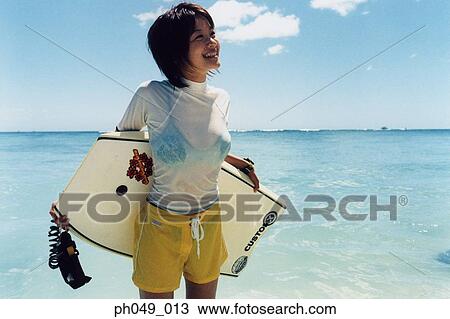 Stock Image - Young woman at a beach, holding paddleboard . Fotosearch